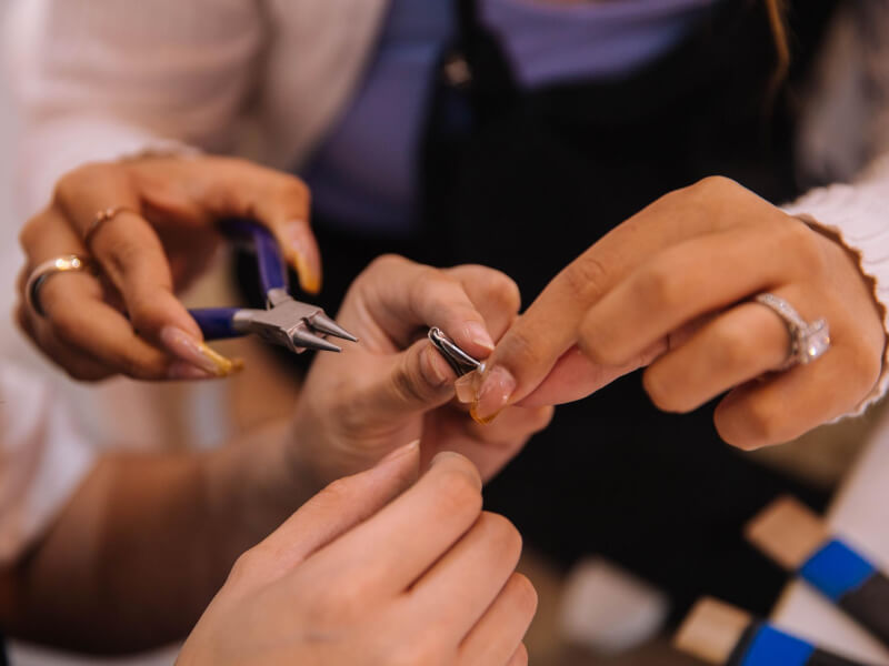 Close up of two people using needle nose pliers to shape precious metal jewellery